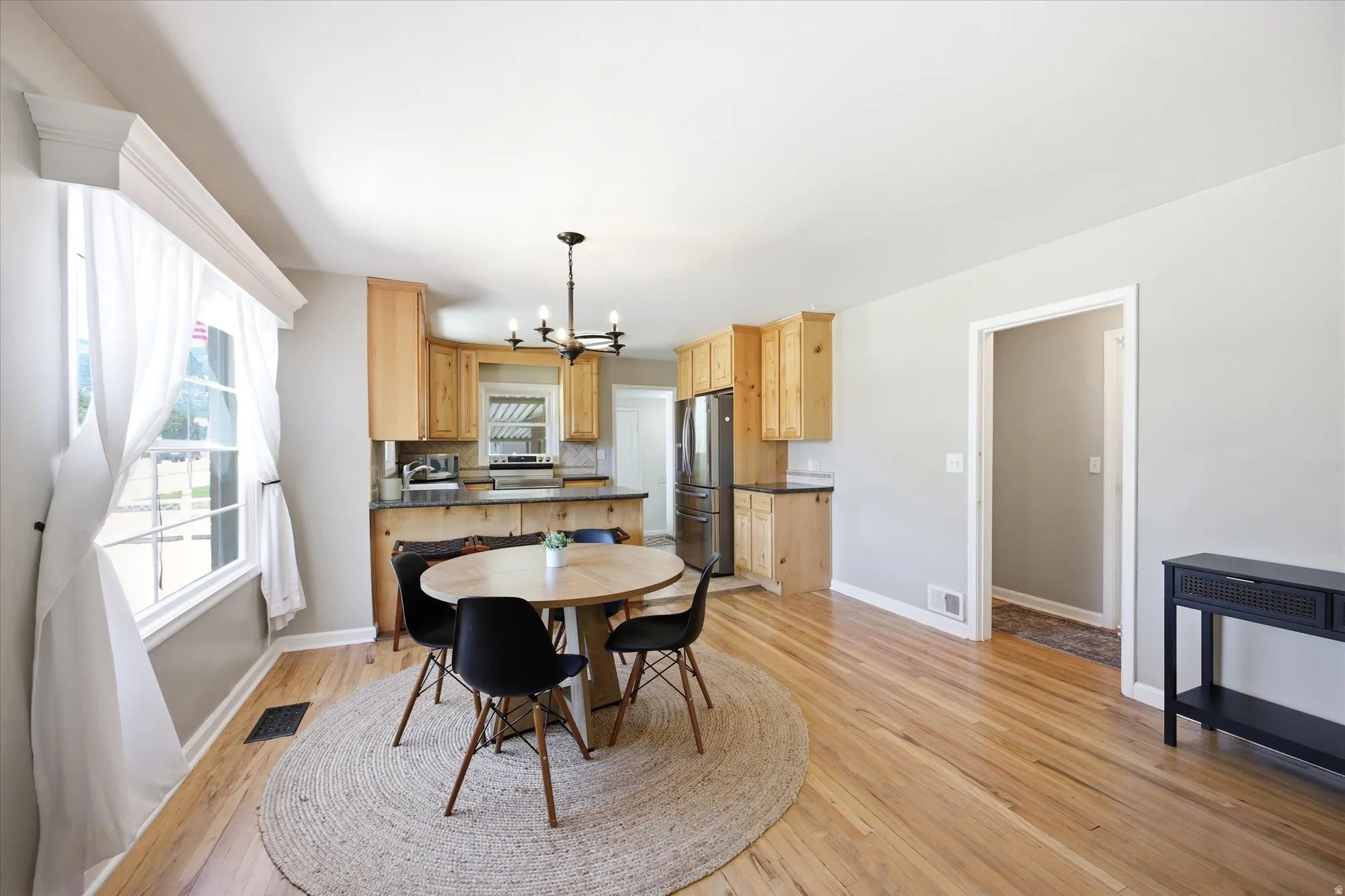 Open-concept living space featuring wood-finish flooring, a kitchen with natural wood cabinetry and stainless steel appliances, and a modern chandelier