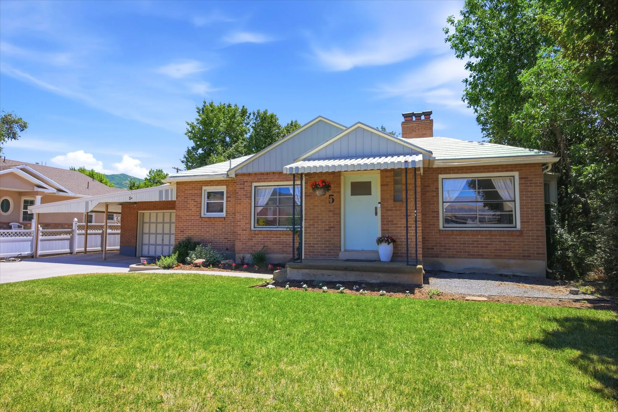 Brick exterior featuring a light blue front door with a striped awning, a manicured front lawn, and an attached carport