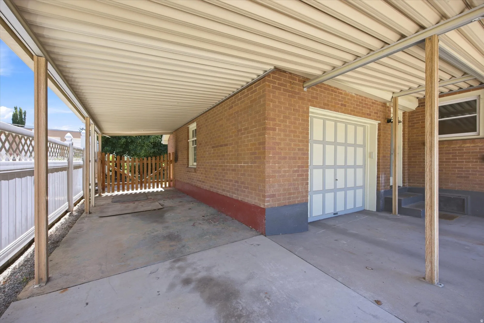 Covered carport with concrete flooring, brick exterior, and a paneled garage door