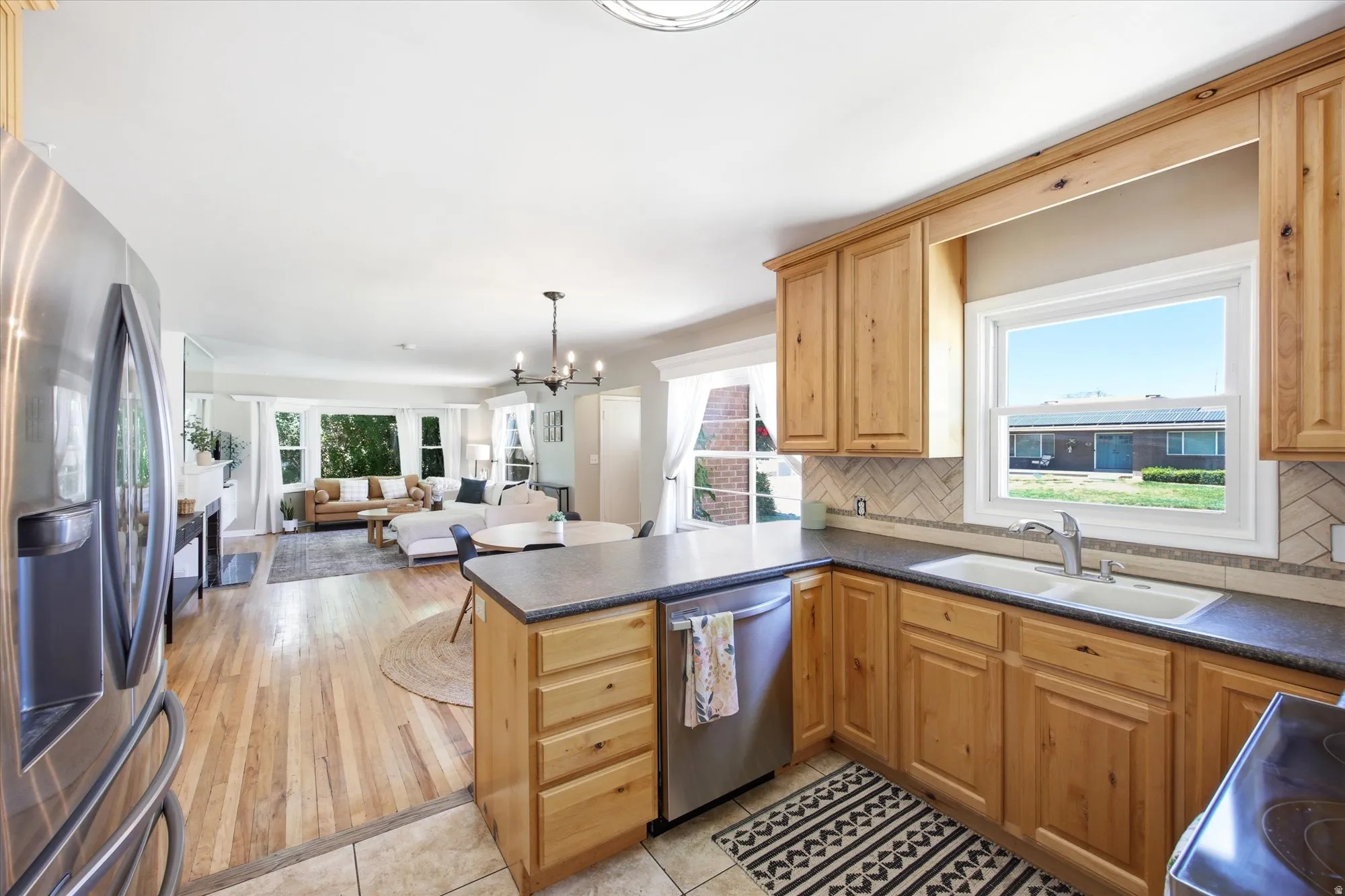 Kitchen featuring wood cabinetry, stainless steel appliances, dark countertops, and a tile backsplash, with a bright window overlooking the exterior