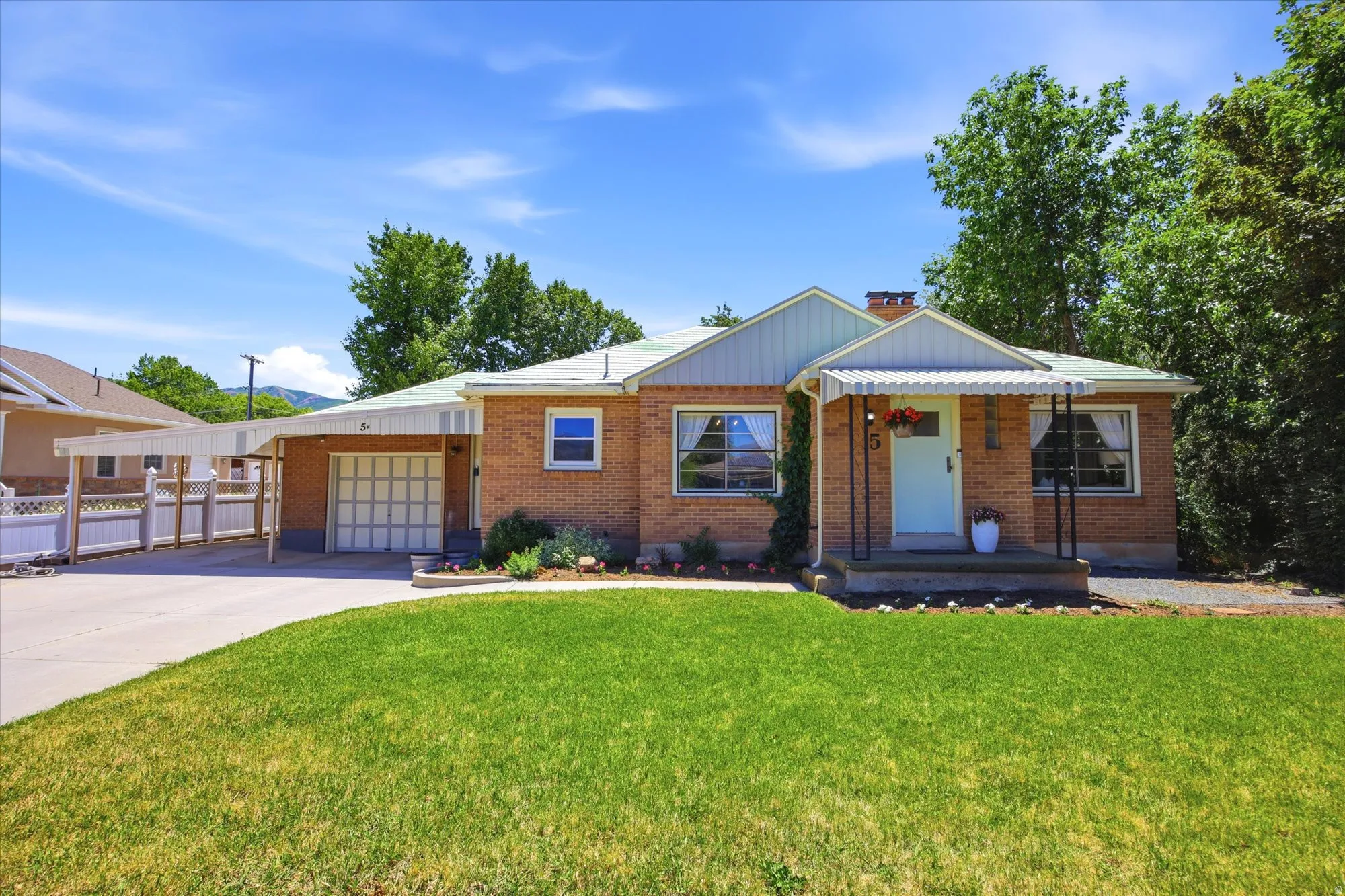 Brick exterior residence featuring a light blue front door, covered porch with black metal railings, an attached garage, and an extended carport