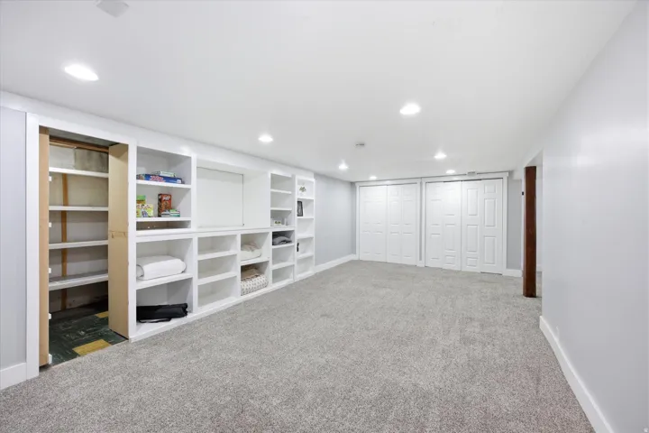 Spacious room featuring extensive built-in shelving, plush gray carpeting, recessed lighting, and white bi-fold closet doors