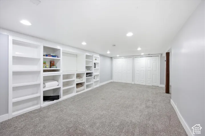 Expansive room featuring a wall of built-in white cabinetry and shelving, recessed lighting, light gray carpeting, and multiple white bi-fold closet doors