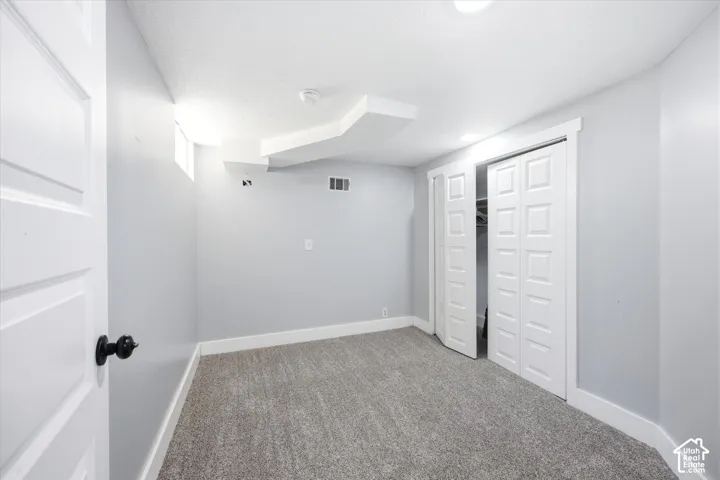 Carpeted room featuring light gray walls, white baseboards, and a white six-panel door with a black knob