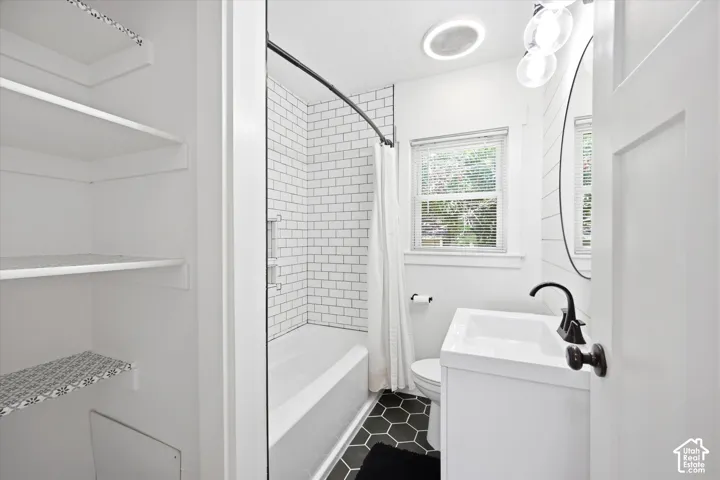 Bathroom featuring a white subway tile shower surround, dark hexagonal floor tiles, a white vanity with a rectangular sink, matte black faucet, and a round wall-mounted mirror