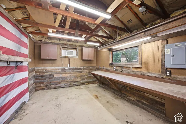 Utility room featuring a concrete floor, exposed wood beam ceiling, linear fluorescent lighting, and a built-in workbench with storage