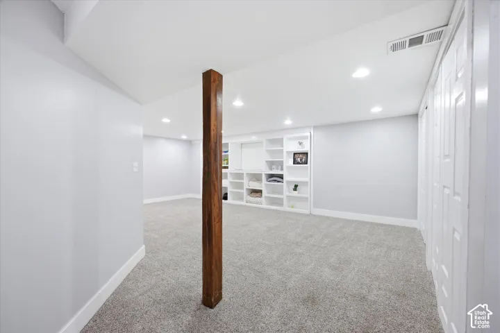 Spacious room featuring light gray walls, recessed lighting, built-in shelving, gray carpeting, and white trim