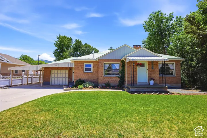 Brick exterior residence featuring a light blue front door, covered porch with black metal railings, an attached garage, and an extended carport