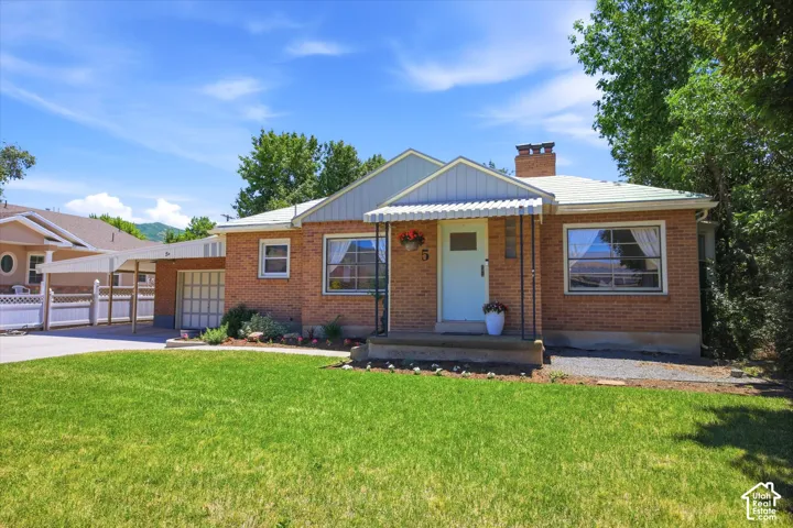 Brick exterior featuring a light blue front door with a striped awning, a manicured front lawn, and an attached carport