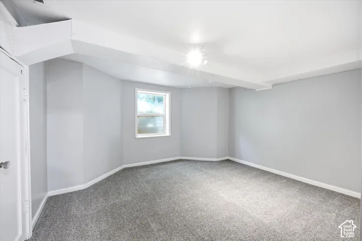 Room featuring light gray walls, gray carpet, a single window, white trim, and a white ceiling with exposed beams