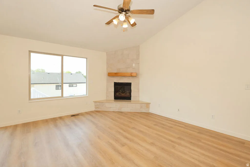Vaulted ceiling great room featuring wood-finish flooring, a corner fireplace with a stone surround, and a natural wood mantel