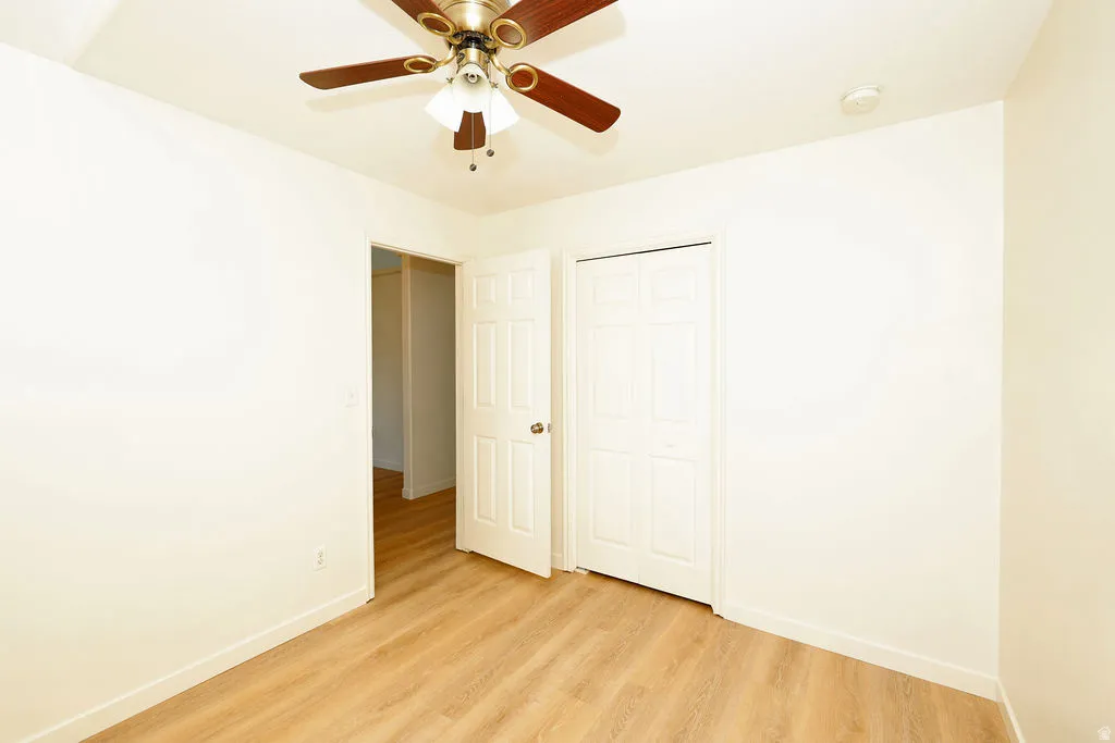 Bright room featuring wood-finish flooring, a ceiling fan with light fixture, white baseboards, and two white panel doors