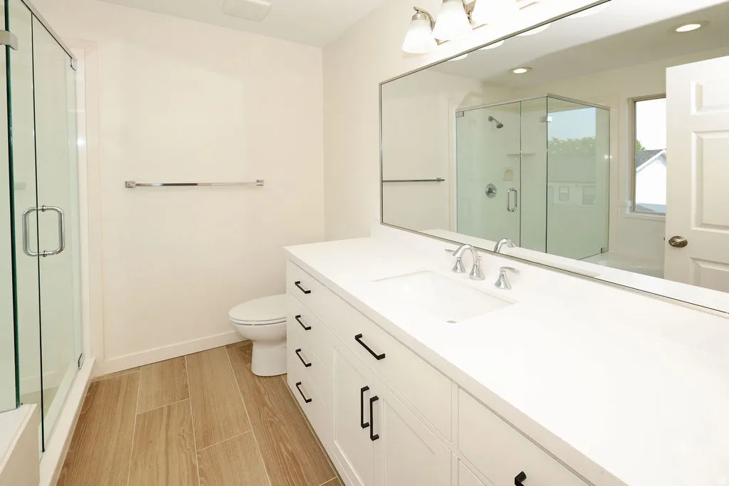 Spacious bathroom featuring a double vanity with white cabinetry, light countertops, and wood-finish tile flooring