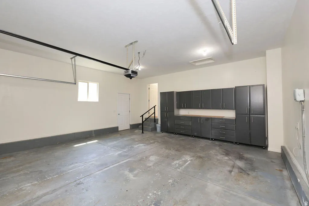 Spacious garage featuring extensive built-in gray cabinetry with wood-finish countertops, concrete flooring, and a single window for natural light