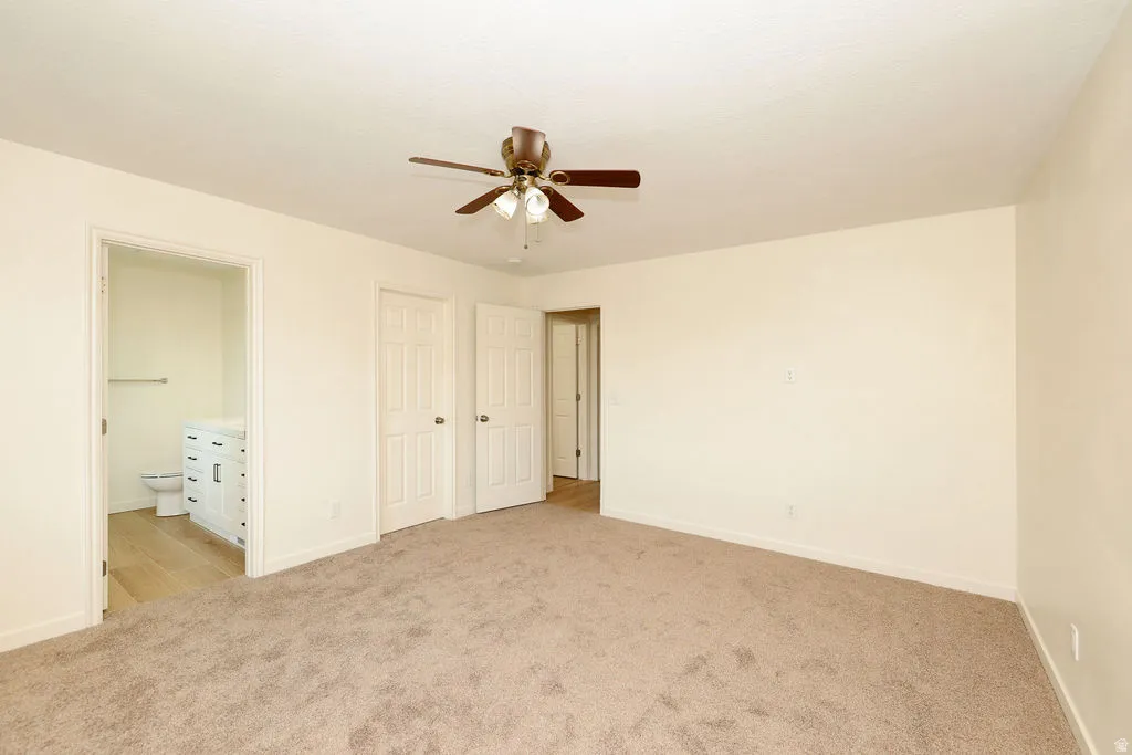 Spacious room with plush carpet flooring, a ceiling fan with light fixture, and neutral wall tones
