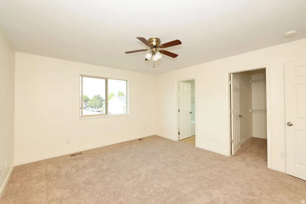 Spacious room featuring neutral carpet, a large window, and a ceiling fan with light fixture