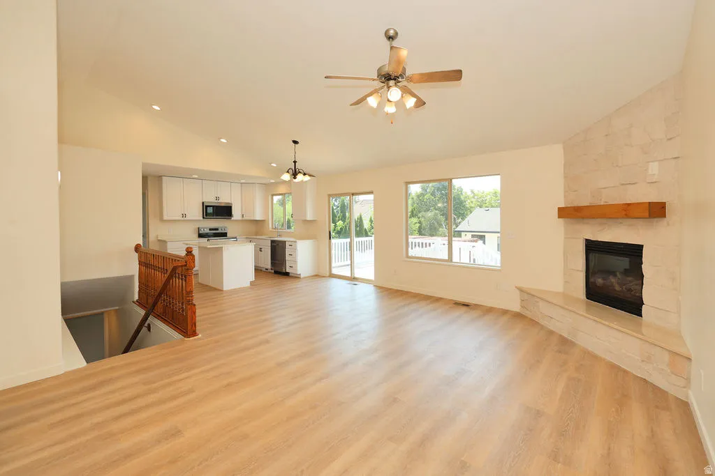 Spacious room featuring wood-finish flooring, a contemporary fireplace with a stone surround and wood mantel, white kitchen cabinetry with a central island, and a sliding glass door opening to an outdoor deck