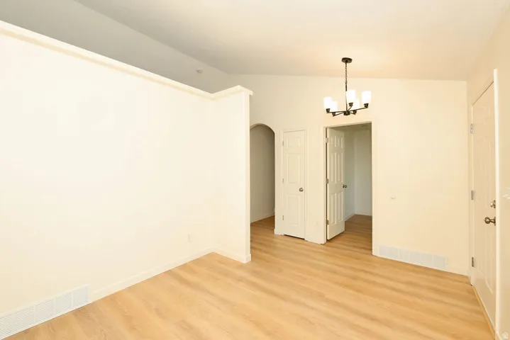 Open-concept living area with wood-finish flooring, a contemporary chandelier, vaulted ceiling, and arched entryway