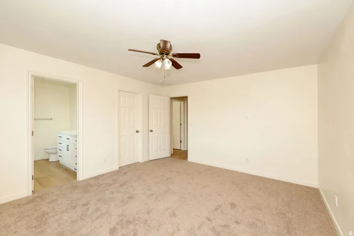 Spacious room with plush carpet flooring, a ceiling fan with light fixture, and neutral wall tones