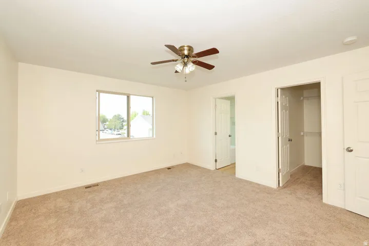 Spacious room featuring neutral carpet, a large window, and a ceiling fan with light fixture