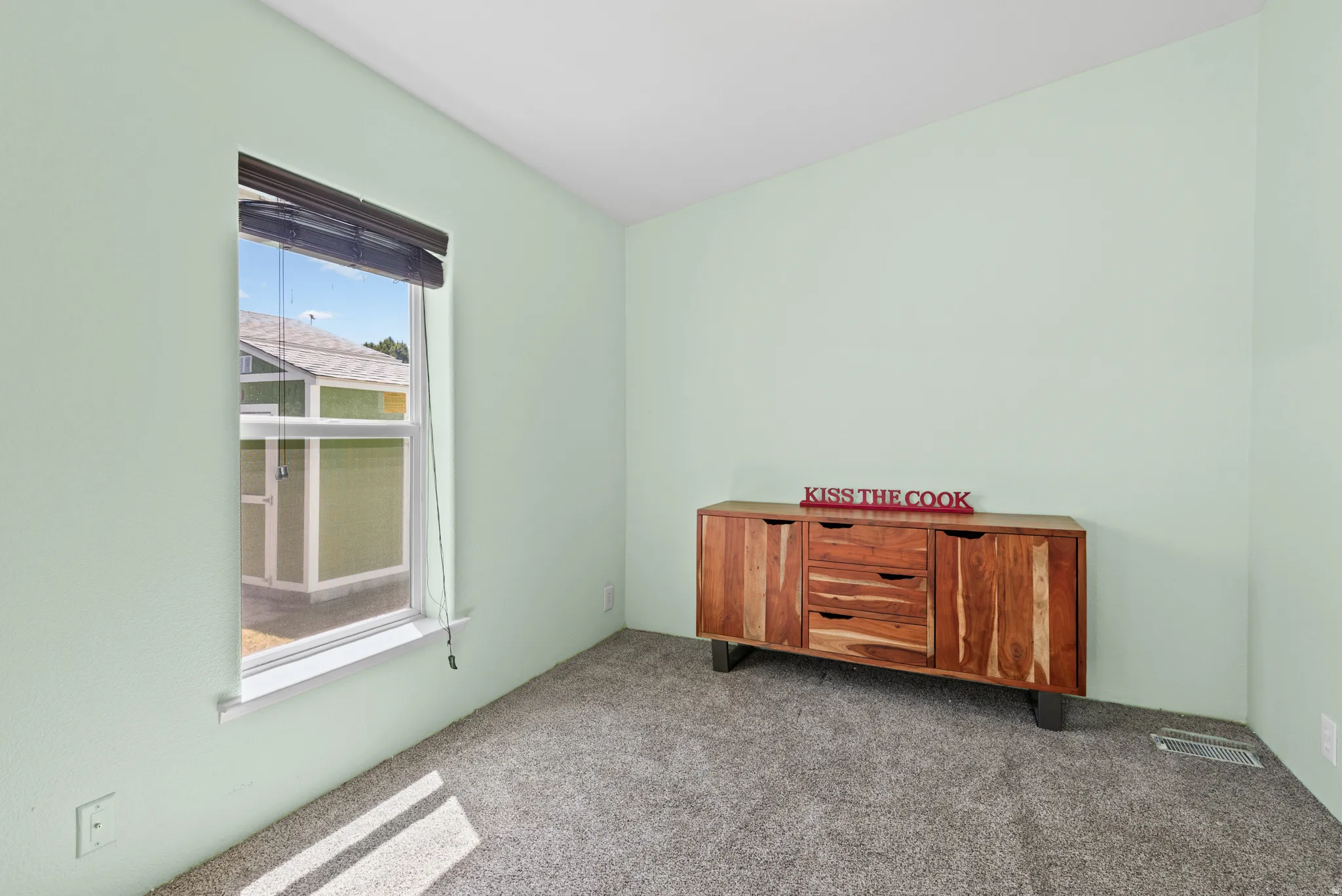 Carpeted interior space featuring light green painted walls and a window with blinds