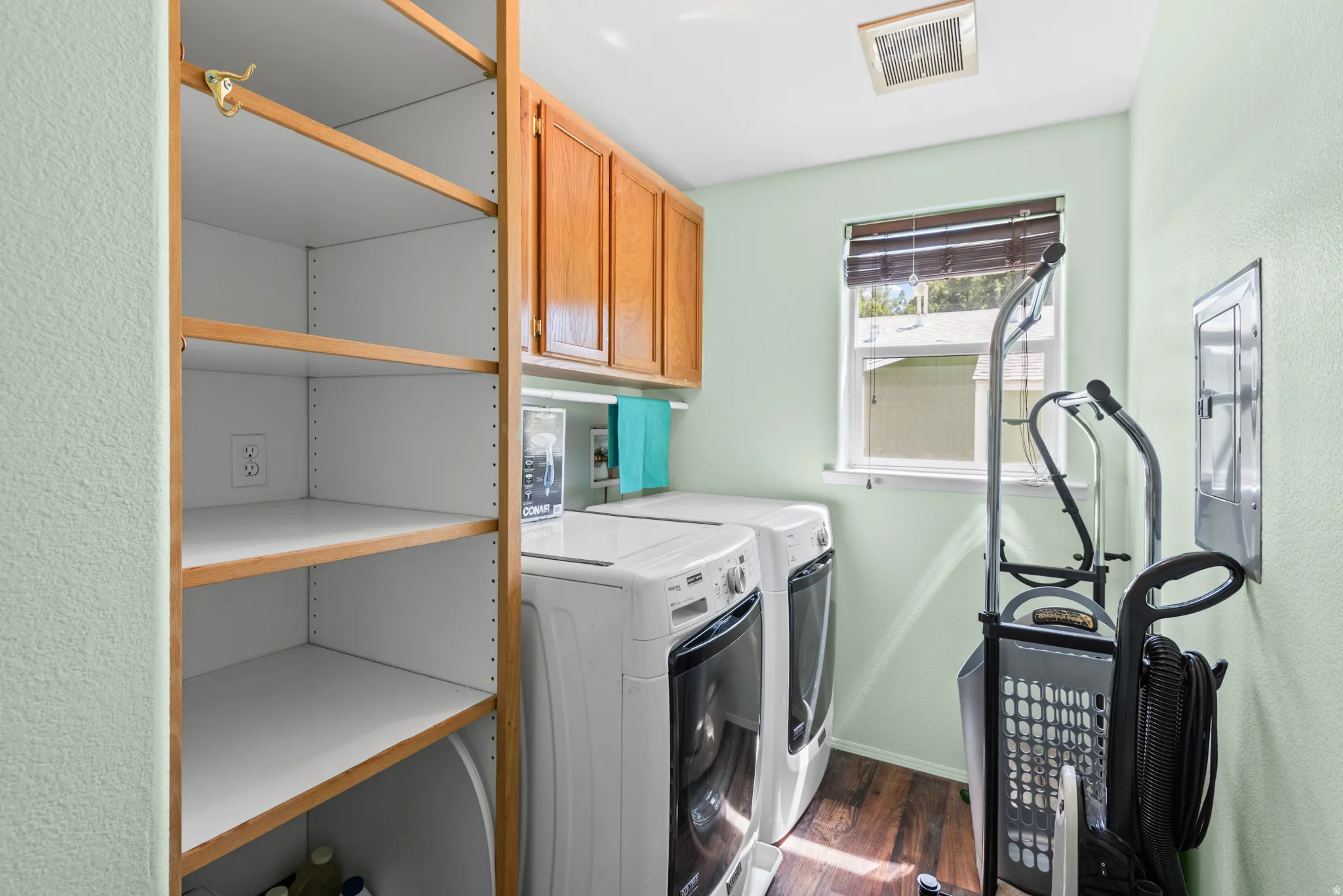Dedicated laundry space featuring built-in shelving, wood-finish flooring, a window with blinds, and overhead cabinetry