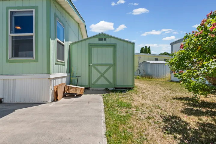 Exterior features include a light green shed with an X-braced door, a concrete patio area, and a green mobile home facade with white trim