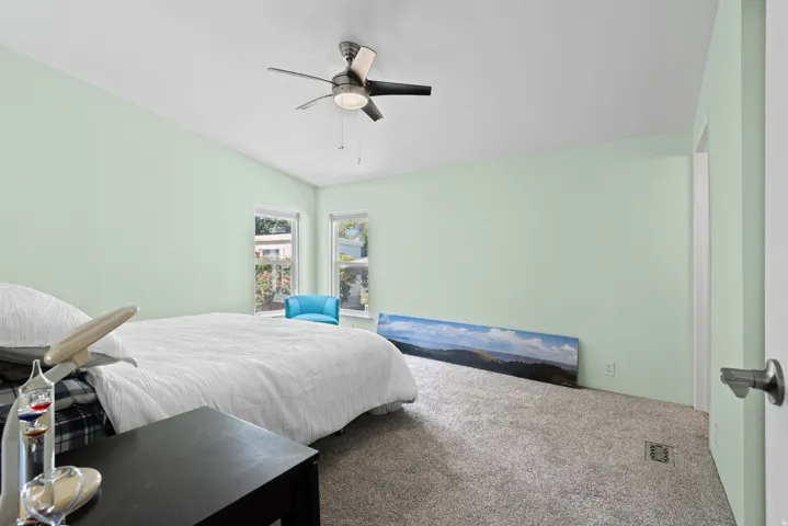 Carpeted bedroom featuring vaulted ceilings, a ceiling fan with integrated lighting, and two windows