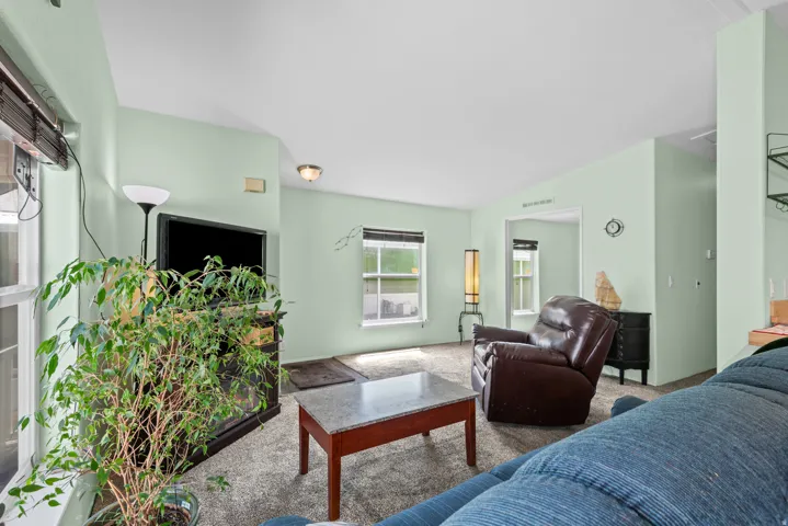 Spacious interior room featuring light-toned walls, textured carpeting, and multiple windows providing natural light