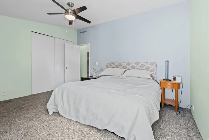 Carpeted room featuring a ceiling fan with integrated lighting, a light blue accent wall, and bi-fold closet doors