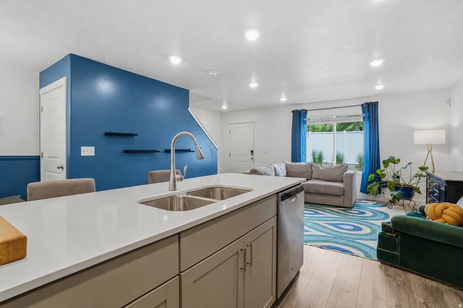 Kitchen island featuring a double-basin stainless steel sink with a high-arc faucet, light gray cabinetry, and a light-toned countertop