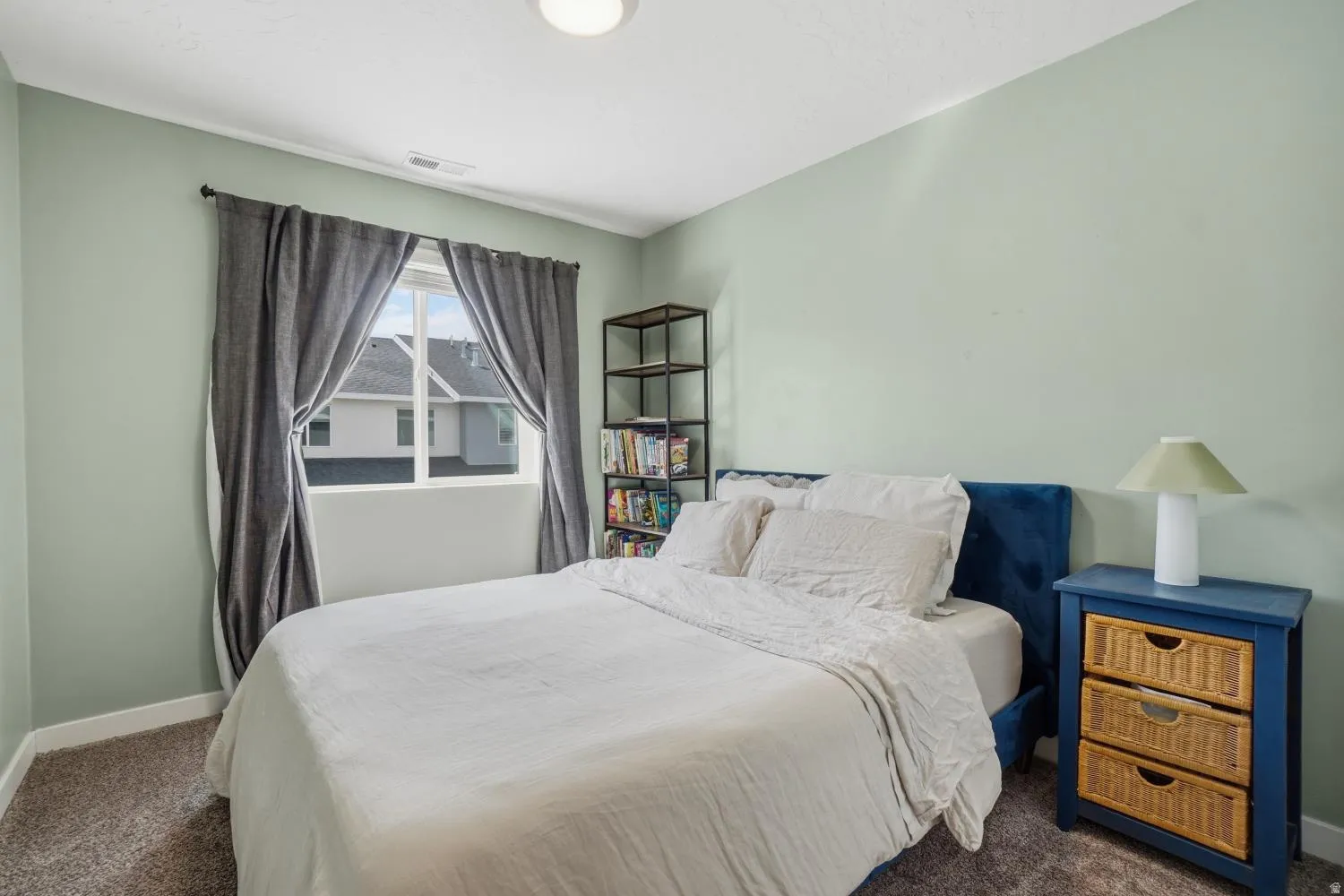 Spacious interior room featuring light green walls, a window with dark drapery, and textured carpeting
