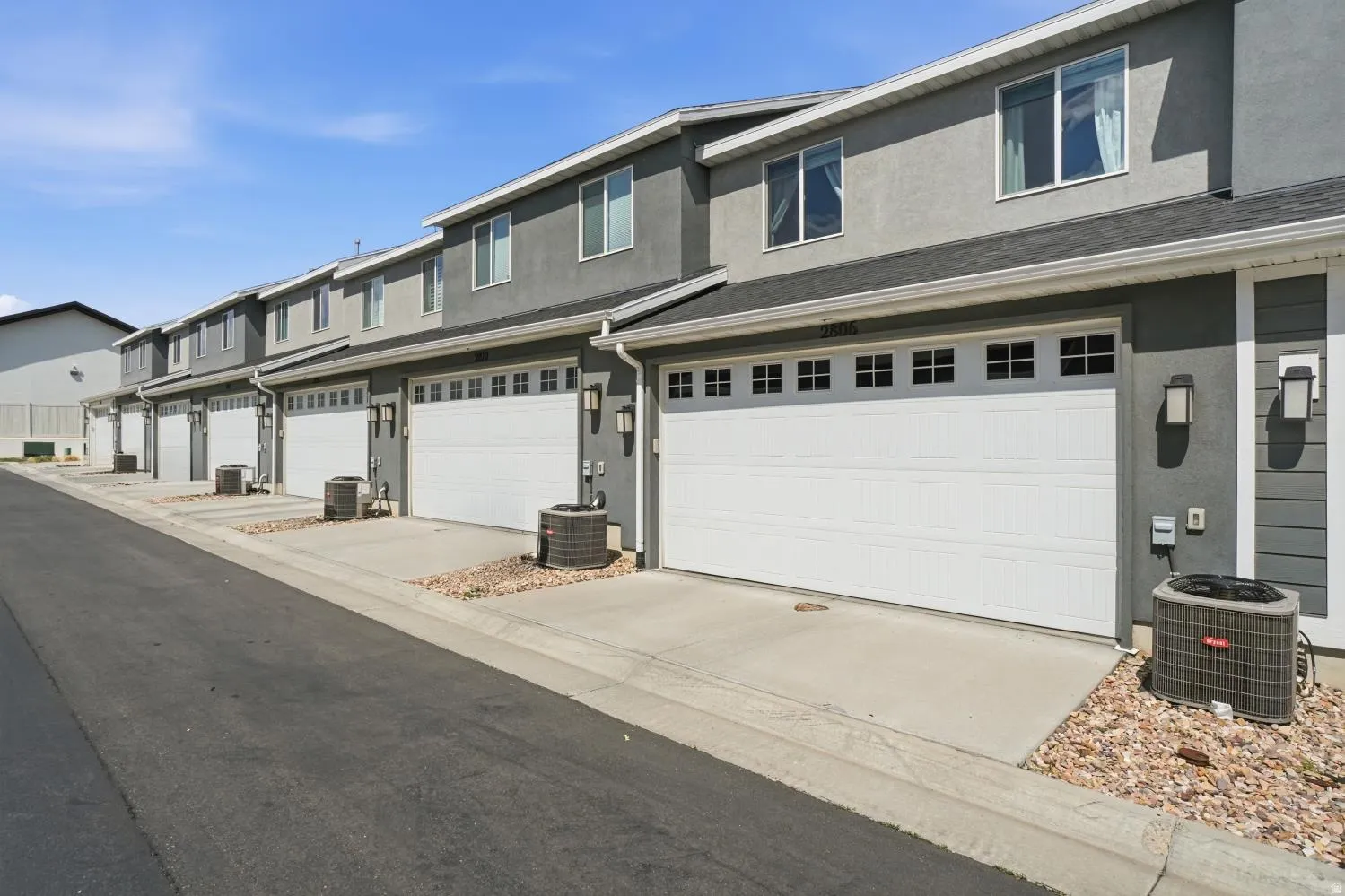 Row of townhomes featuring stucco and siding exteriors, individual two-car garages with window accents, and concrete driveways