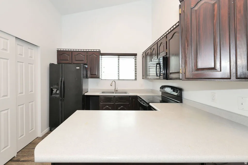Kitchen featuring wood-finish cabinetry, light-toned countertops, black appliances, a double-door refrigerator, and a stainless steel sink with a gooseneck faucet