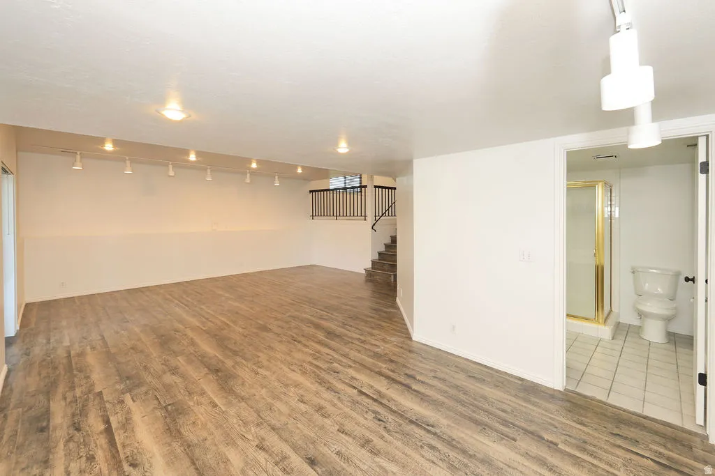 Spacious room featuring wood-finish flooring, white walls, and track lighting