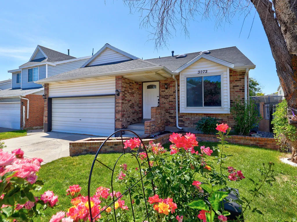Brick facade home featuring an integrated garage, a white front door, and a bay window with white siding
