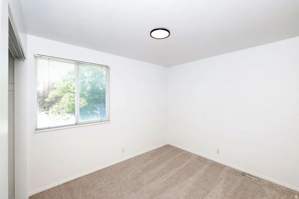 Bright room featuring a window with horizontal blinds, neutral-toned carpet, white baseboards, and a contemporary ceiling light fixture