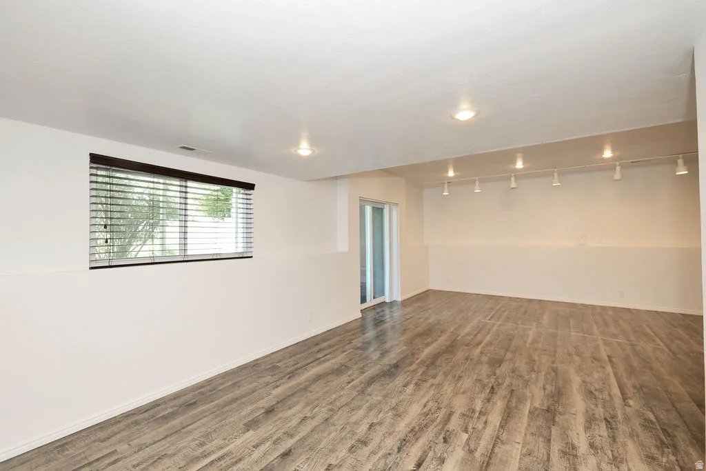 Spacious room featuring wood-finish flooring, a window with blinds, recessed lighting, and track lighting