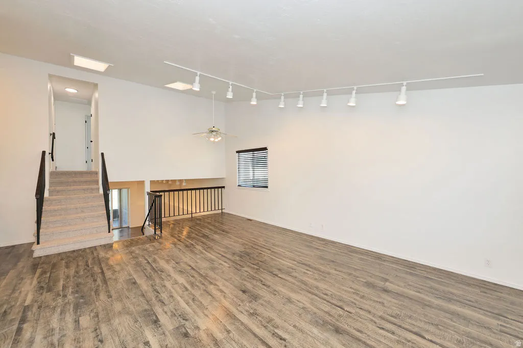 Open-concept living area featuring wood-finish flooring, a contemporary track lighting system, and a ceiling fan