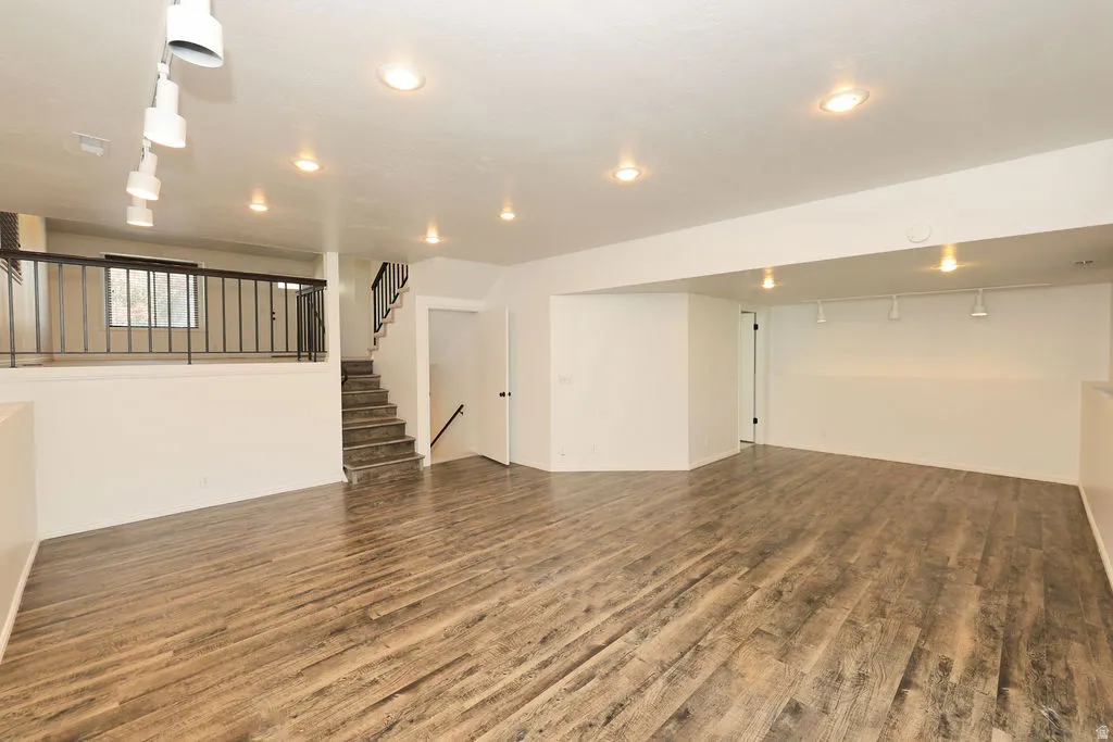 Spacious finished area featuring wood-finish flooring, recessed lighting, track lighting, a staircase with black railings, and a landing with coordinating black railings