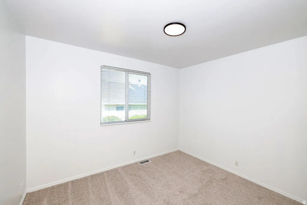 Light-filled room featuring neutral wall paint, a window with blinds, a ceiling-mounted light fixture, and carpet flooring
