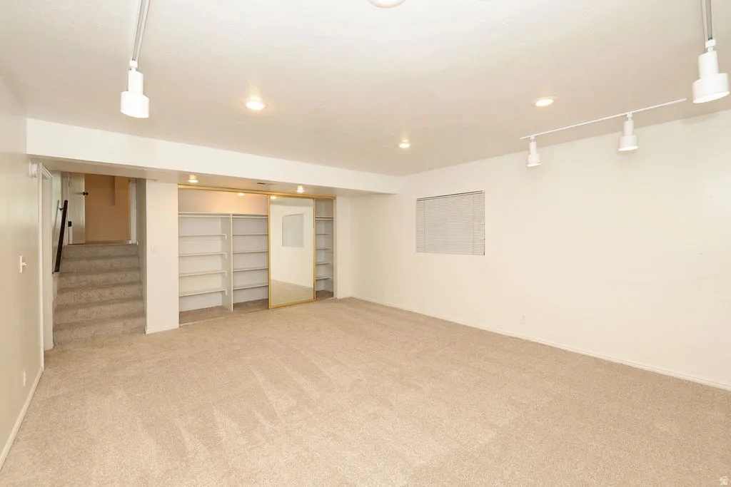 Carpeted room featuring built-in shelving with mirrored sliding doors, track lighting, recessed lighting, and a window with blinds