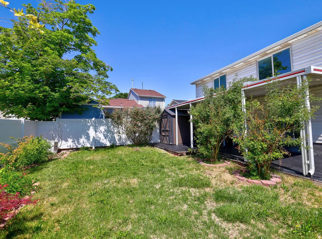 Expansive backyard featuring a white vinyl privacy fence, mature perimeter trees, and a garden shed with a covered walkway