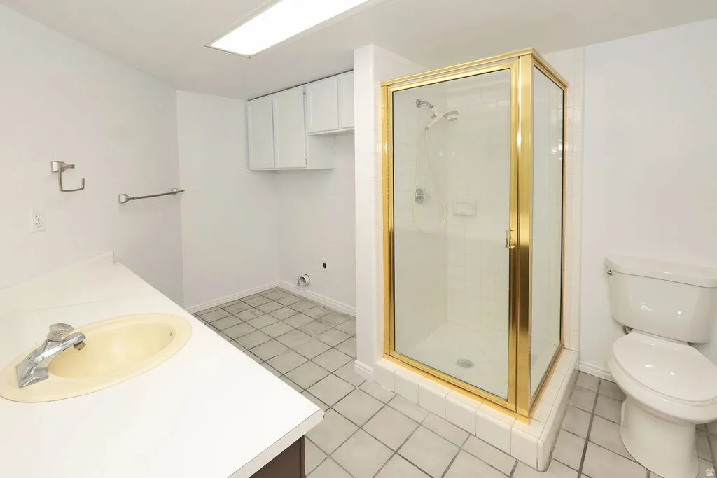 Bathroom featuring a gold-framed glass shower enclosure, white vanity countertop with integrated sink, white toilet, and grid-patterned floor tiles