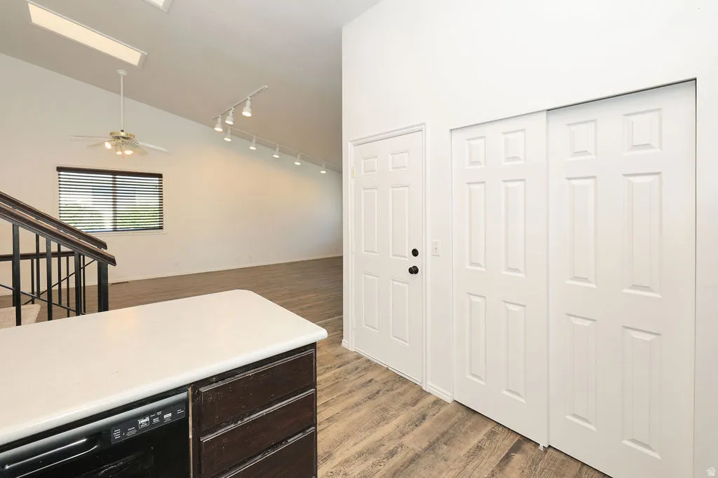 Interior space featuring a white countertop with integrated dishwasher, wood-finish flooring, and a dark wood-finish staircase with black spindles