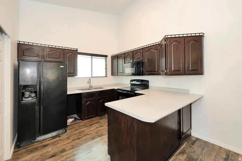 Kitchen featuring dark wood-finish cabinetry, light-toned countertops, and black appliances