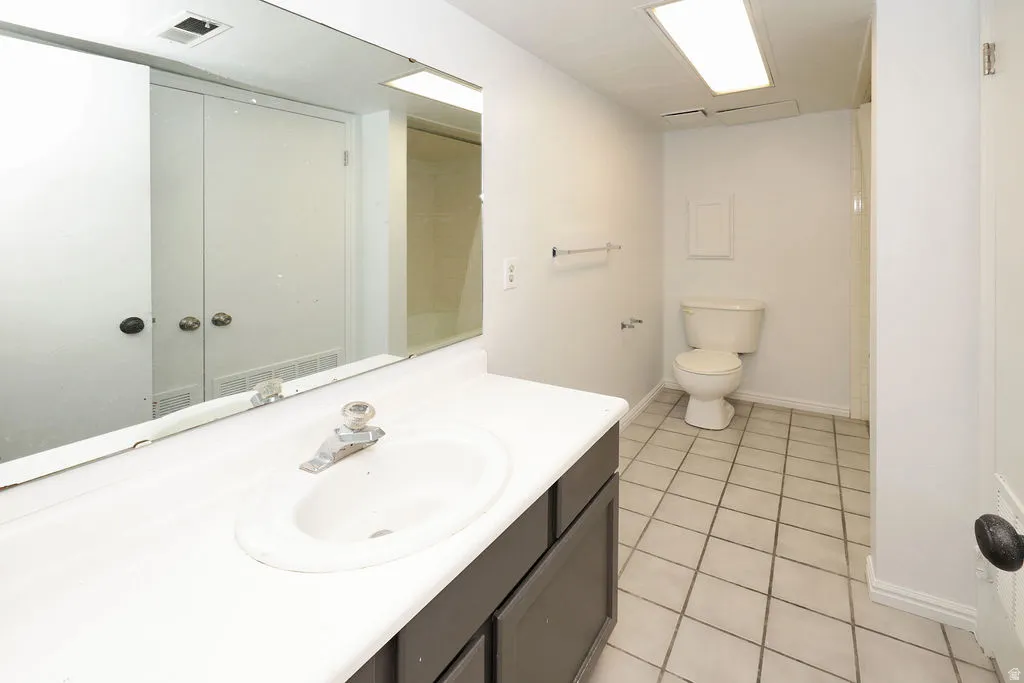 Bathroom with a vanity featuring a white countertop and dark cabinetry, a white toilet, and square tile flooring