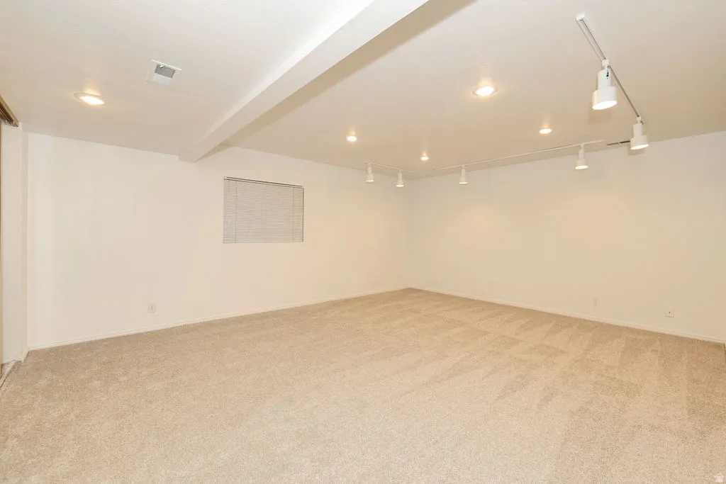 Spacious room featuring neutral carpeting, recessed ceiling lights, track lighting, and a horizontal window with blinds