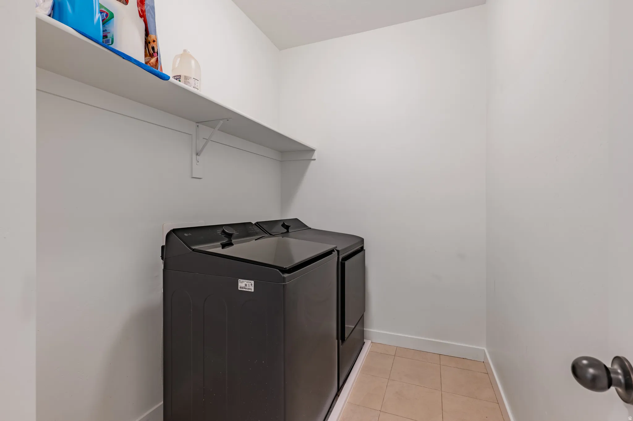 Laundry area featuring a built-in white shelf and neutral tile flooring