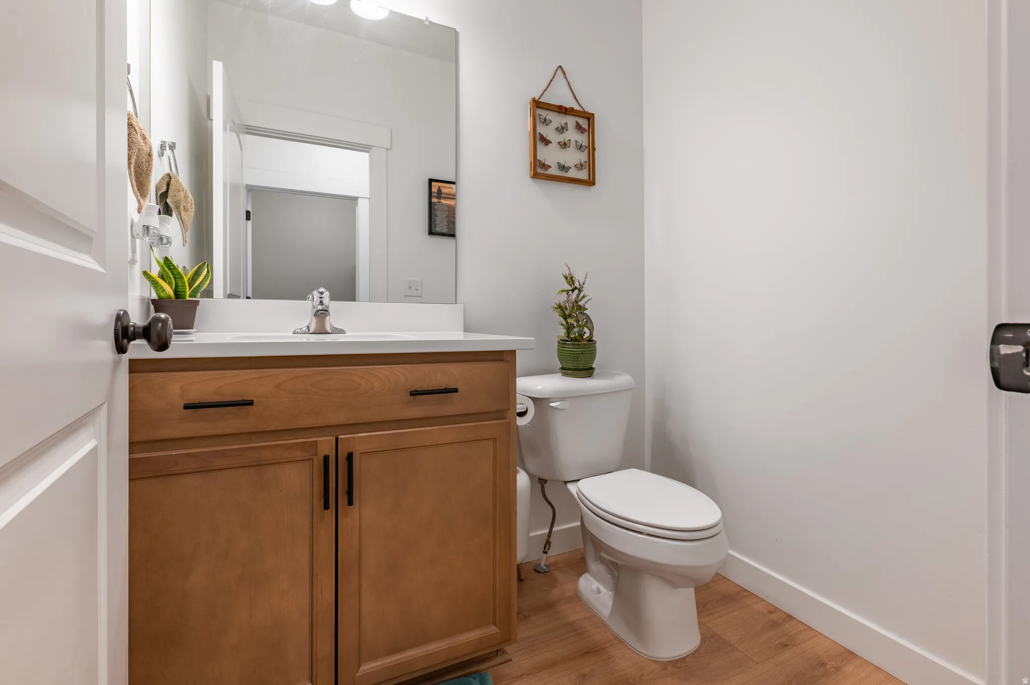 Powder room featuring a wood-finish vanity with a white countertop and undermount sink, a large wall-mounted mirror, and wood-finish flooring